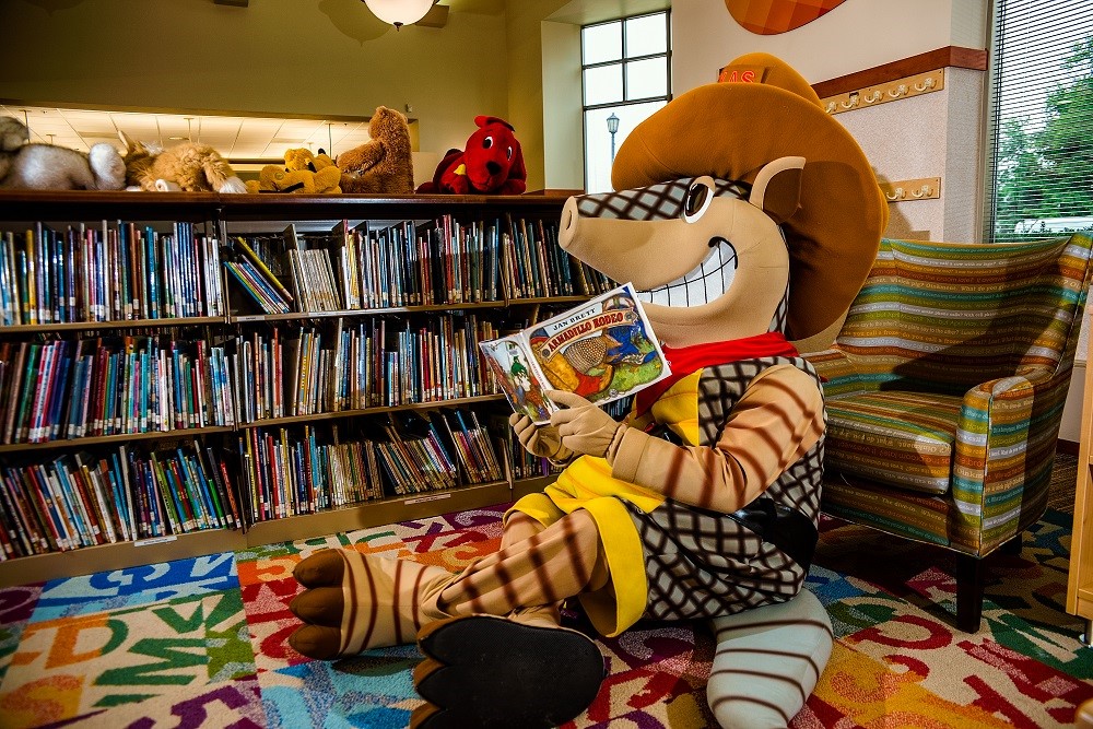 Andy the Armadillo reading a book in a library