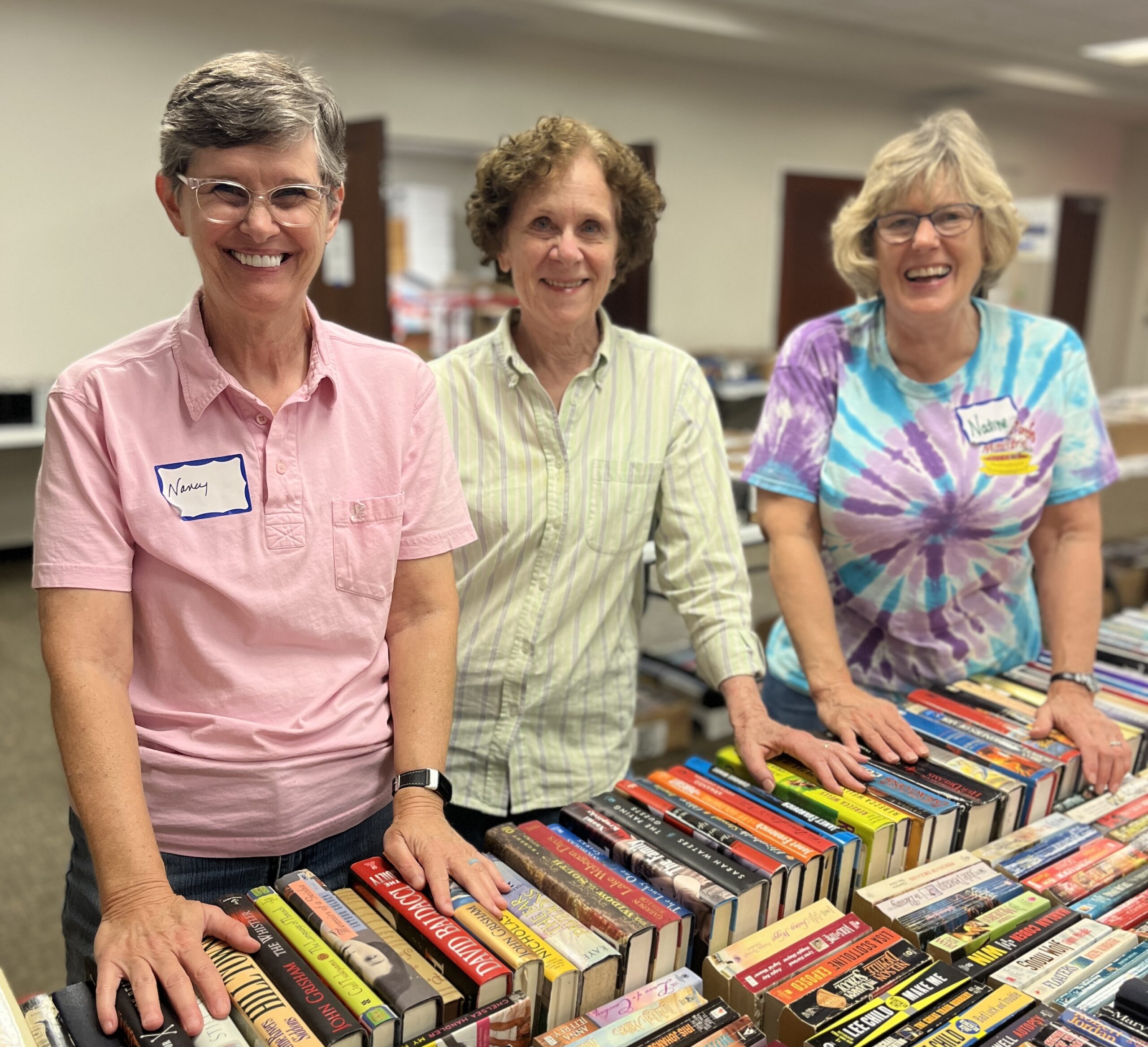 3 women smiling in front of tables with used books