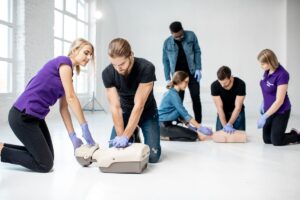 Two men in black t-shirts practicing CPR on test dummies.