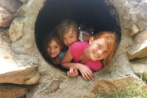 three children smiling and poking out of a cave