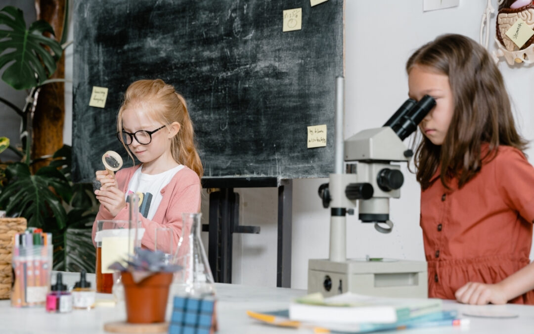 Two preschool girls looking into microscopes in a science lab setting.