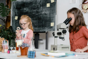 Two preschool girls looking into microscopes in a science lab setting.