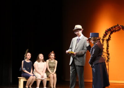 Three female acresses listening to a man in a suit read from a card