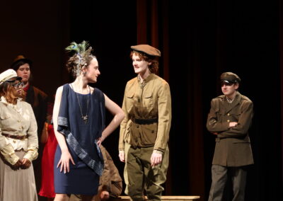 Two actors, one in uniform and the other in a dress, having a conversation in a group