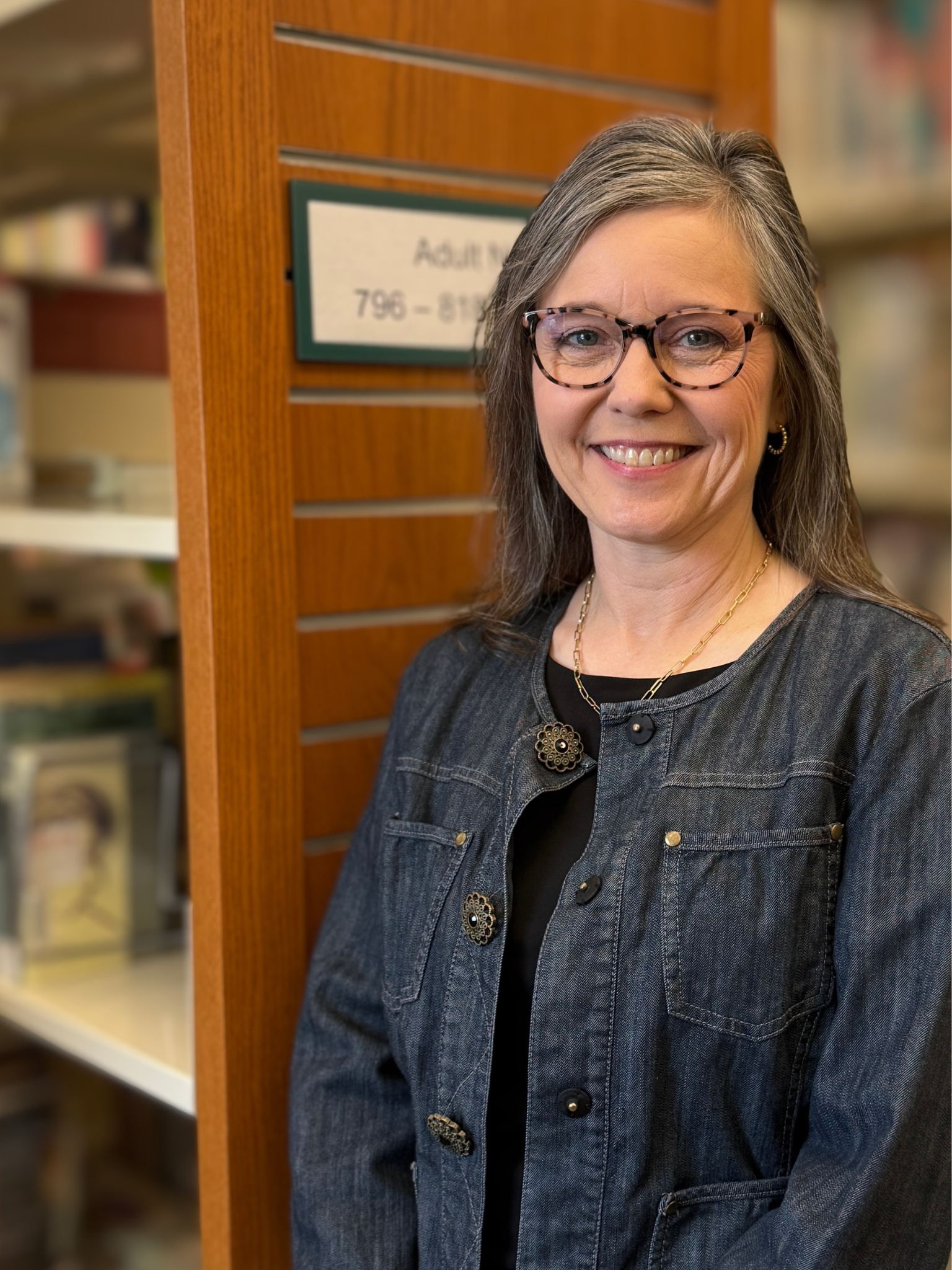 A photo of Ashley Fowlkes, a smiling woman with glasses and shoulder length dark hair